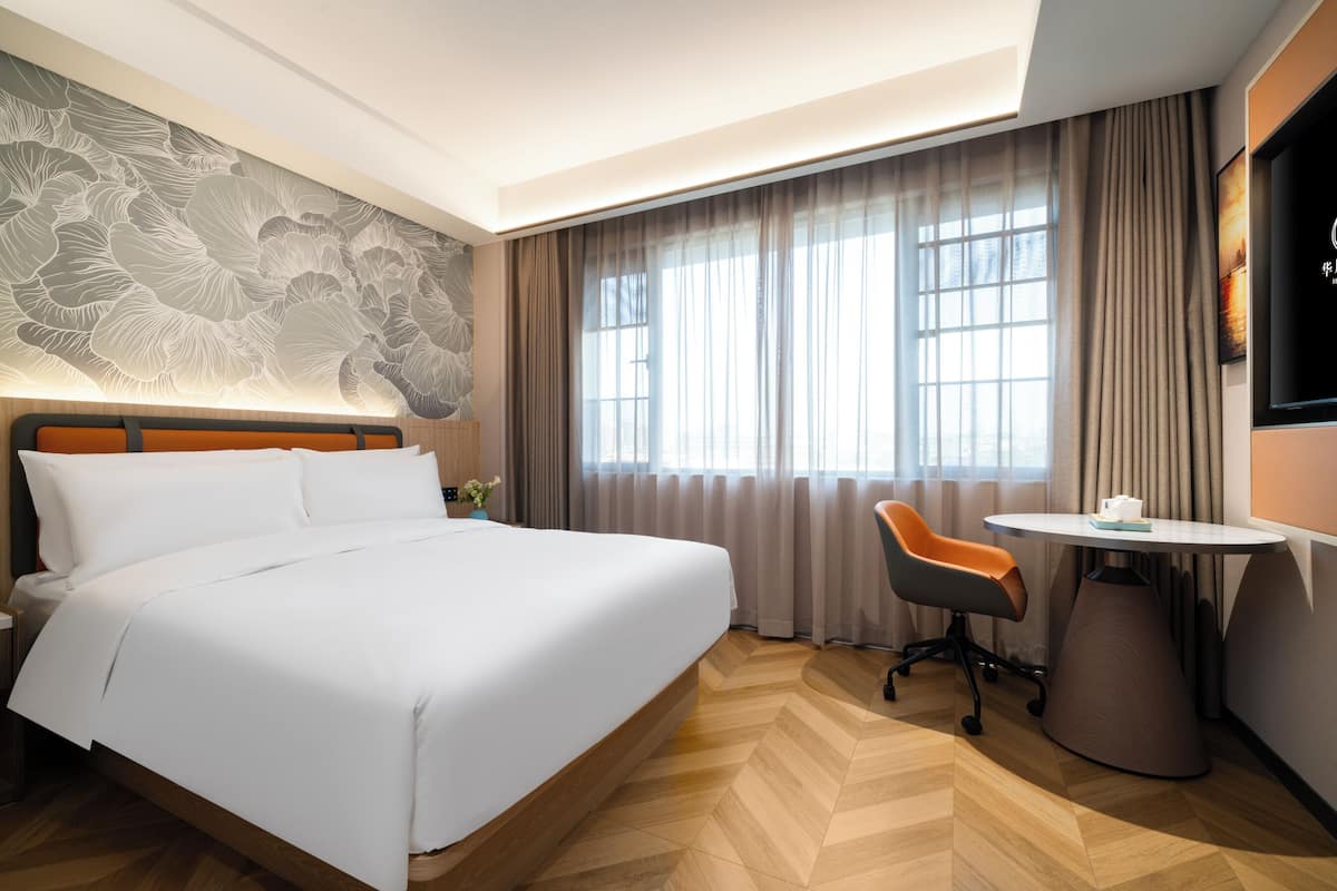 A hotel room with a large bed, a desk with a chair, a TV, and a window with curtains.