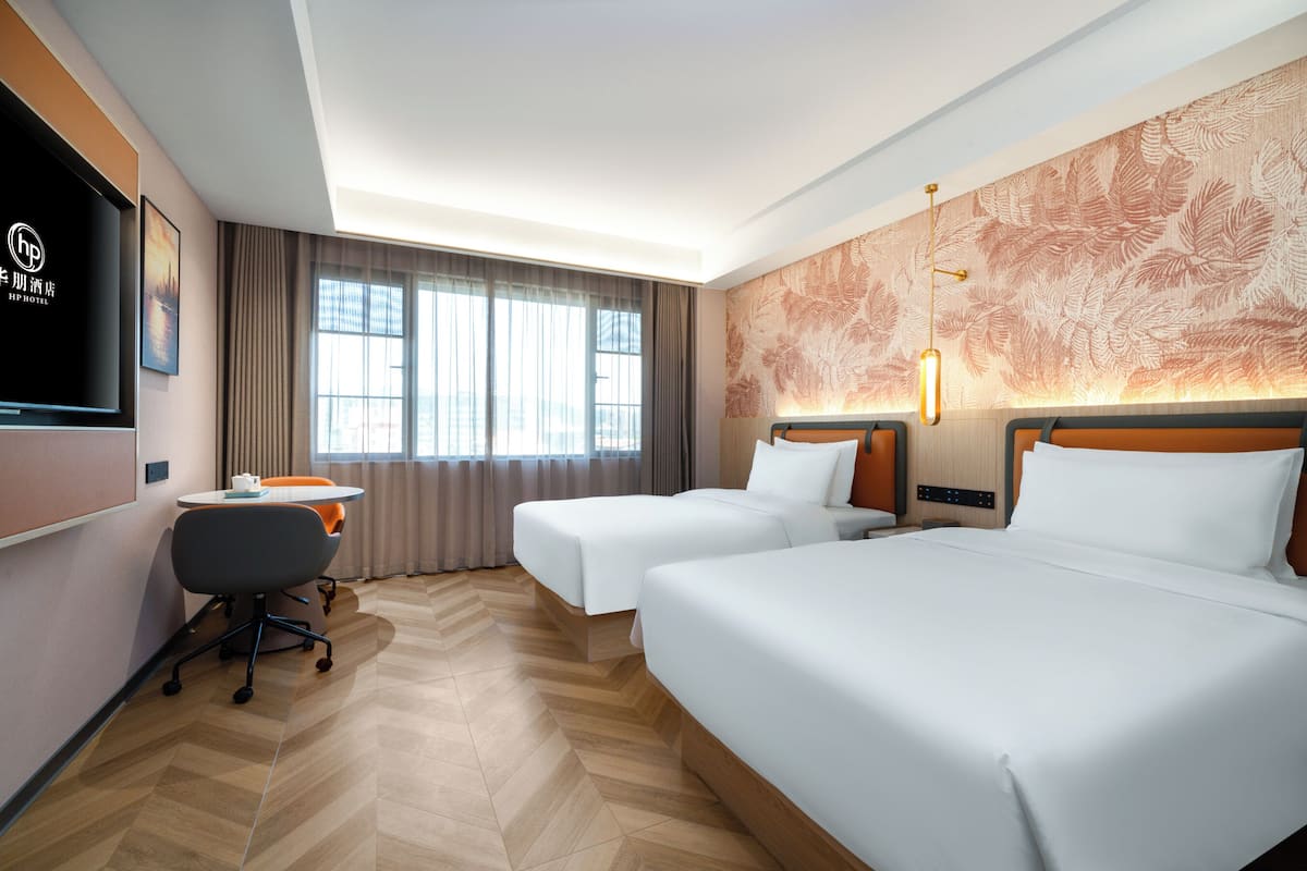 A hotel room with two beds, a desk, and a TV.