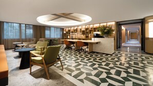 A hotel lobby with a modern design, featuring a reception desk, seating area with chairs, a patterned floor, and a hallway leading to other rooms. - Huapeng International Guangzhou (Guangzhou)