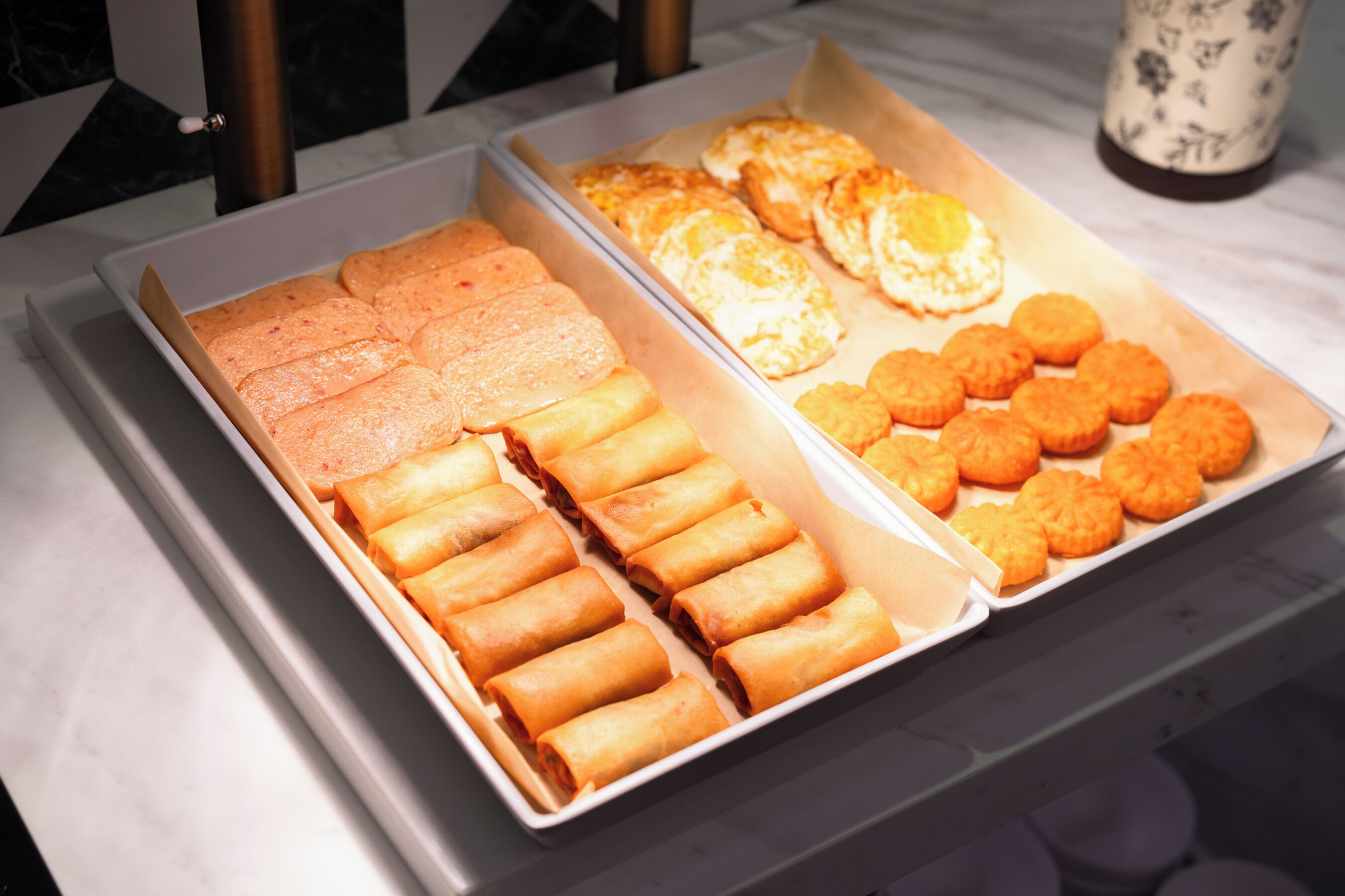 Ein Buffet mit verschiedenen Speisen, darunter Frühlingsrollen, Eierrollen und andere Backwaren.