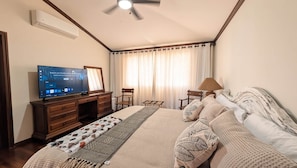 Ein Hotelzimmer mit Bett, Fernseher, Schreibtisch, Stuhl, Lampe und einem Fenster mit Vorhängen.