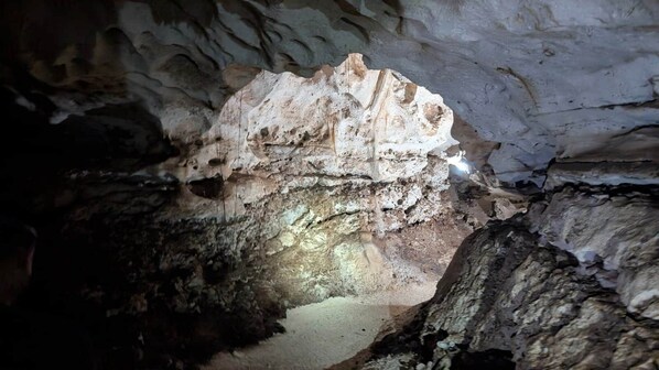 A cave interior with rock formations and a narrow passageway. - Cana Life Luxury | Villa Cueva (Punta Cana)