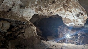 A cave interior with natural rock formations and a visible water stream. - Cana Life Luxury | Villa Cueva (Punta Cana)