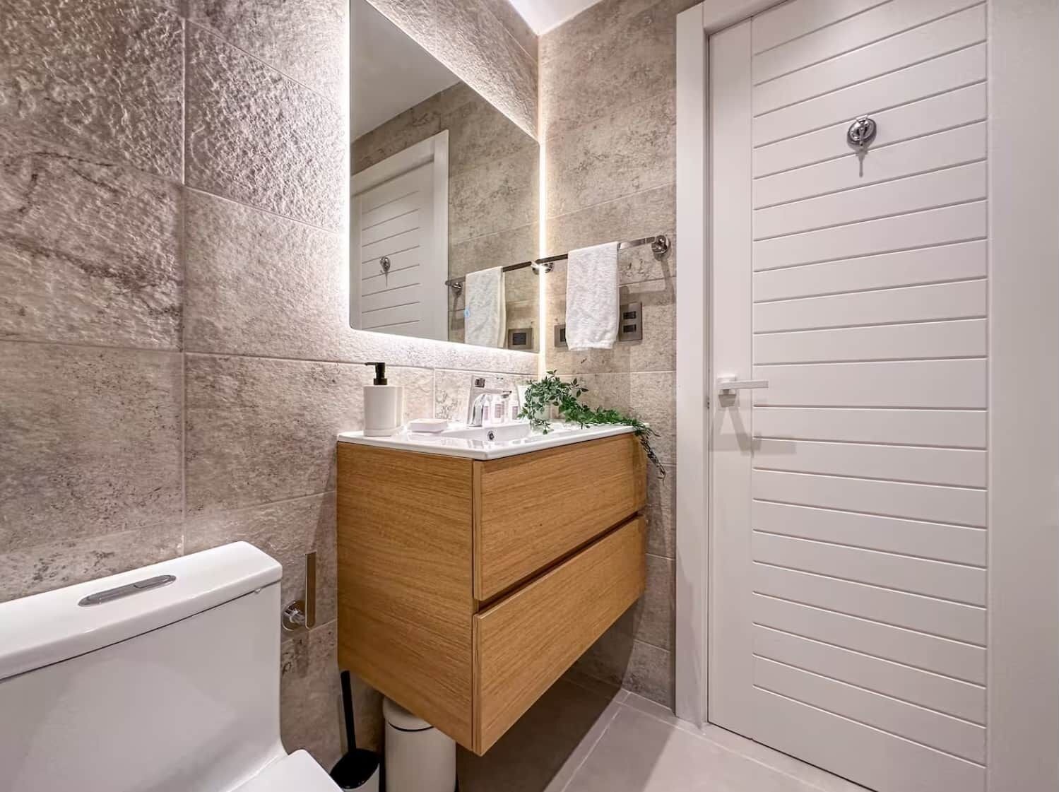 Ein Badezimmer mit einem Holz-Waschtisch, einer weißen Toilette, einem Spiegel und einem Handtuchhalter.