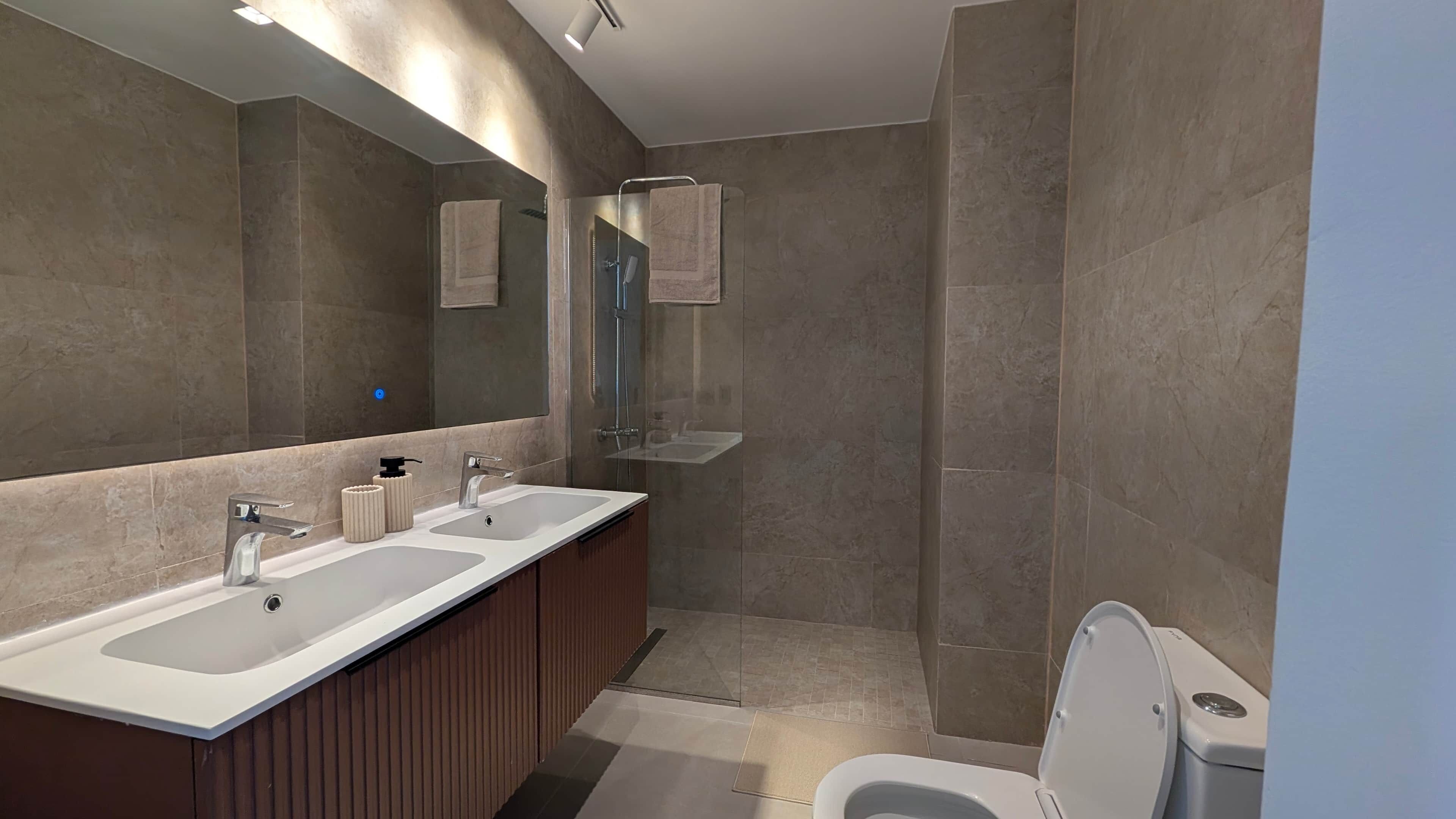 A modern bathroom with a double sink vanity, a glass shower enclosure, and a toilet.