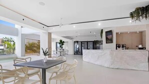 Amplo espaço interno com balcão de recepção, piscina e área de refeições com cadeiras e mesa.