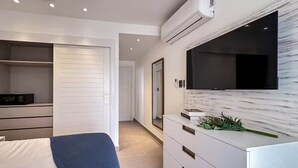 A modern bedroom with a bed, a TV mounted on the wall, and a built-in air conditioning unit. - Cana Life Luxury | Sapphire Sky Pool Penthouse (Punta Cana)