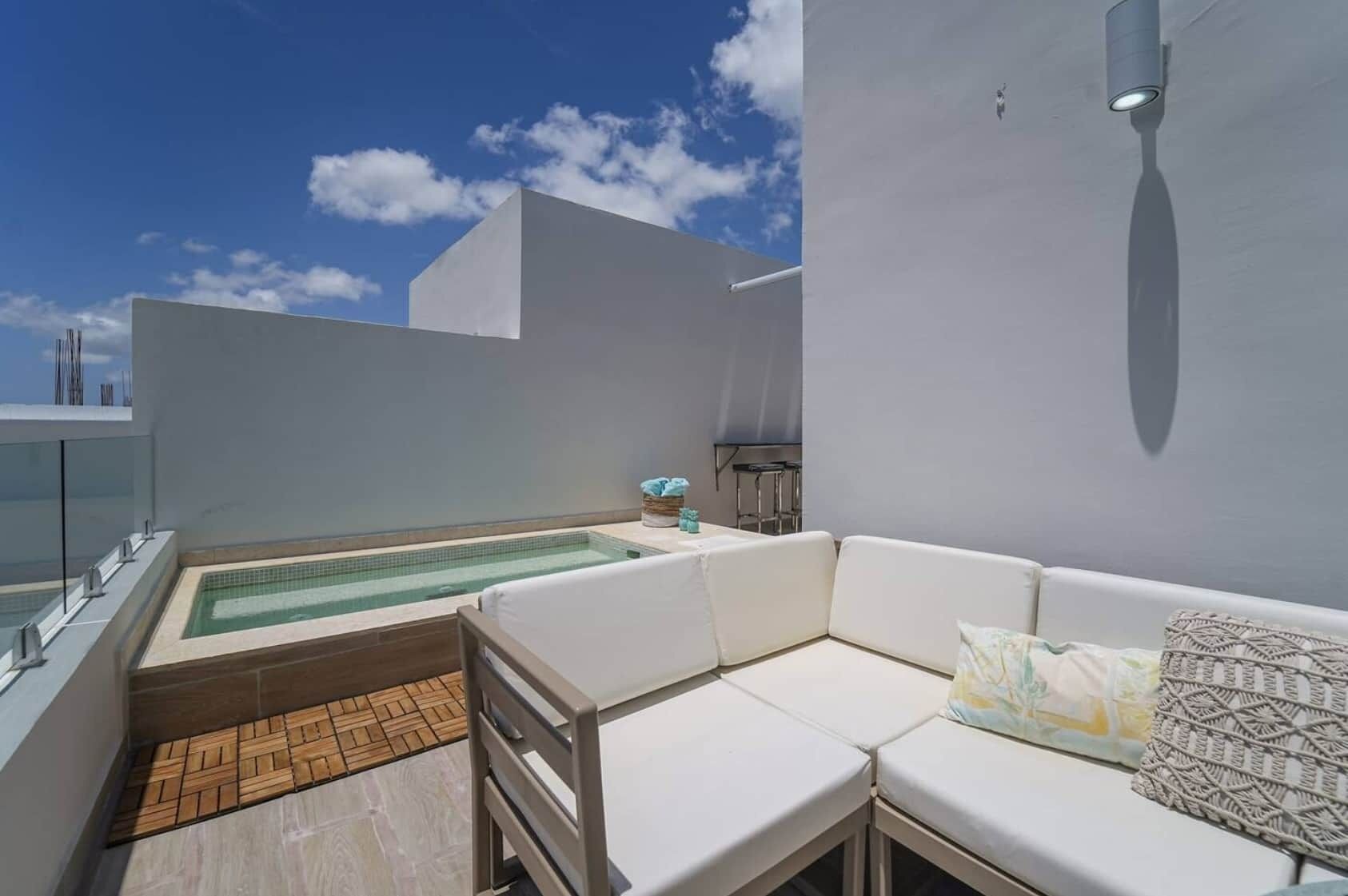 Una terraza en la azotea con piscina, un sofá blanco y una zona de bar.