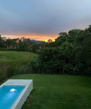 A swimming pool with a stone border, surrounded by a grassy lawn and dense foliage. - Cana Life Luxury Eco | Pineview Jimenoa Villa (Jarabacoa)