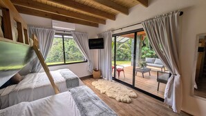 Una habitación con cama, televisor, ventana grande y puerta corrediza de vidrio que da a un espacio exterior.