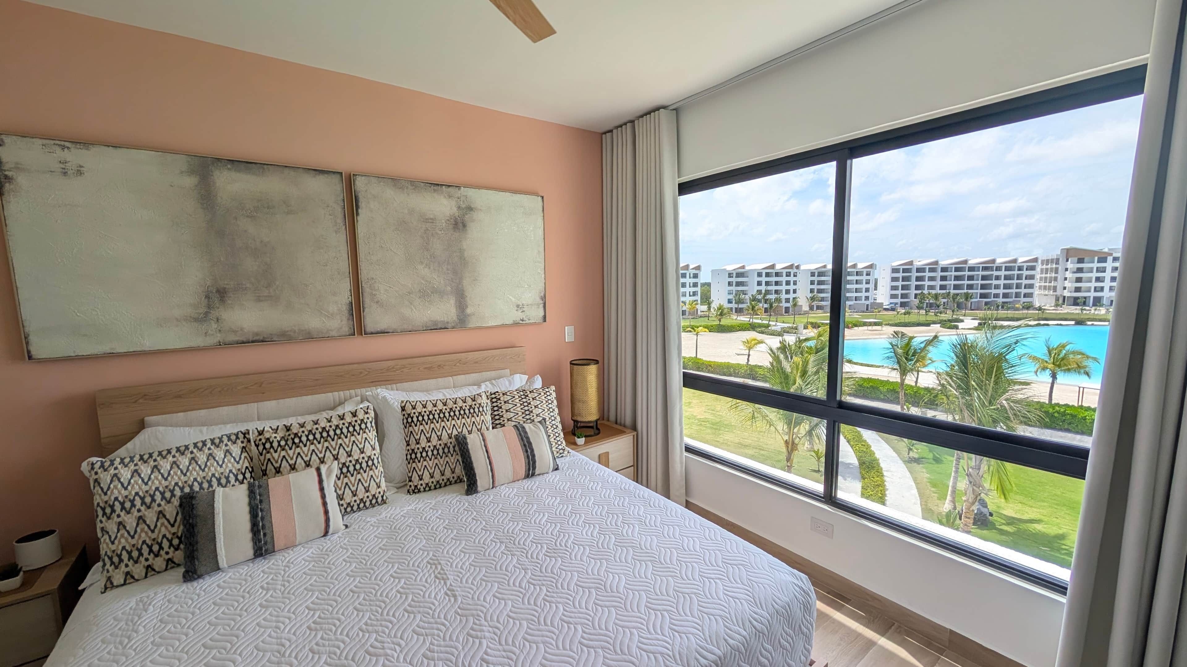 A hotel room with a large bed, a view of a pool, and a balcony.