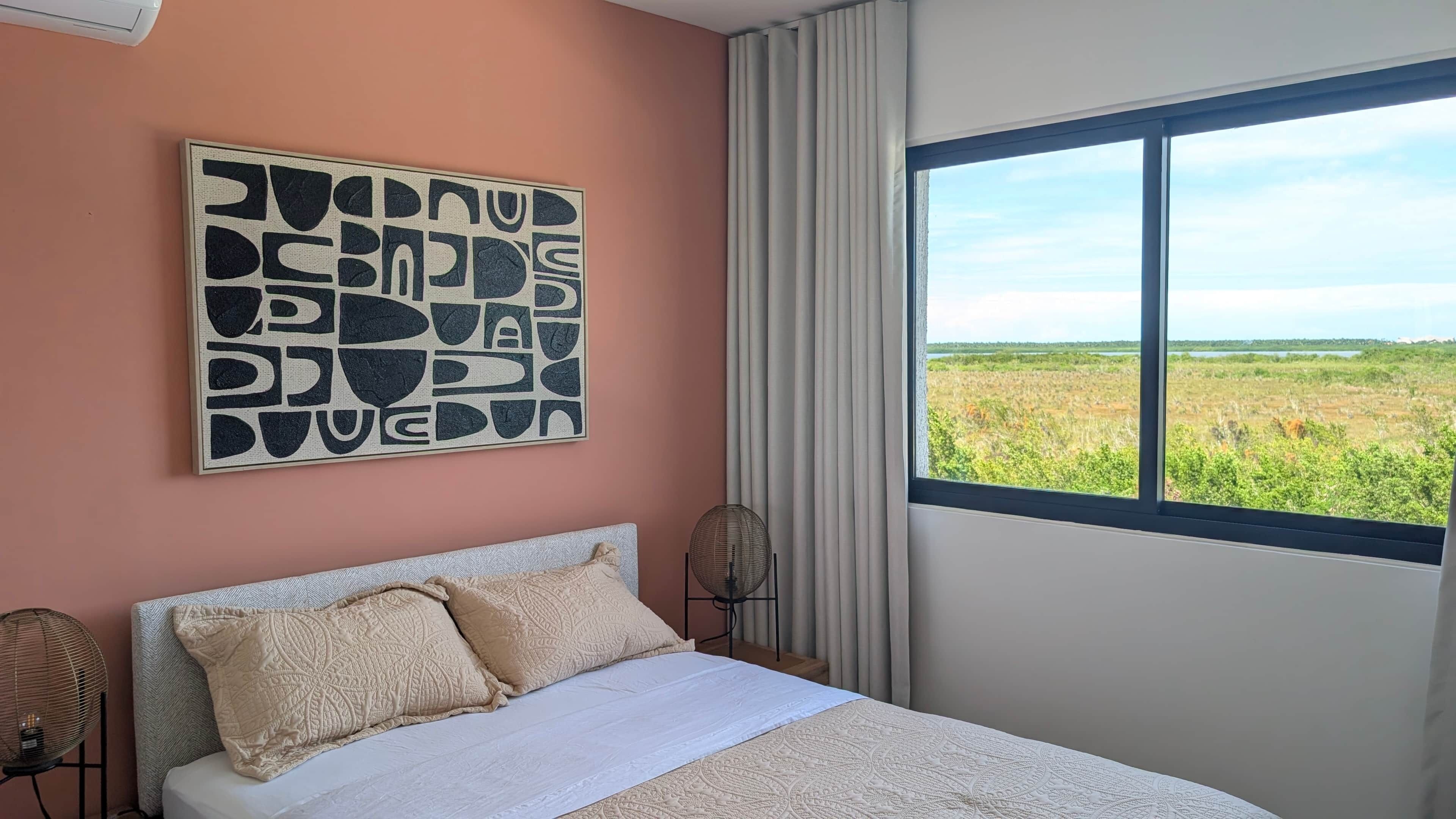 Un dormitorio con cama, un ventanal con vistas al paisaje y una obra de arte en la pared.
