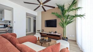 Een moderne woonkamer met een bank, een salontafel, een televisie bevestigd aan een structuurwand en een plafondventilator.