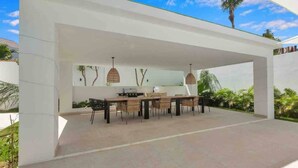 Un patio al aire libre con una mesa y sillas de comedor, una parrilla y una pared con un mural de un árbol.