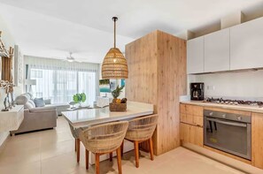 A modern kitchen with a central island, wooden cabinets, a gas stove, and a dining area with wicker chairs. - Cana Life Luxury | Beach Suite (Punta Cana)