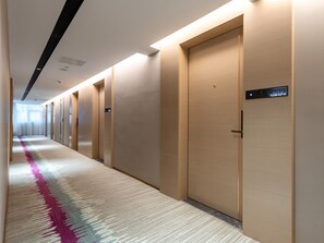 Passadís d'hotel amb sòl de moqueta, portes i un panell digital que mostra el número de habitació 8702.