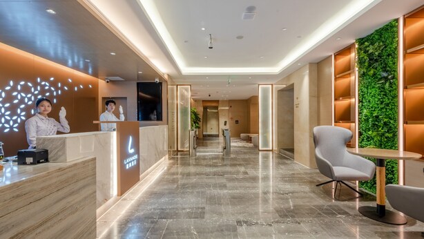 A modern hotel lobby with a reception desk, a seating area, and a green wall. - Lavande International Huawei Guangzhou  (Guangzhou)