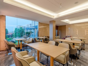 A modern dining area with tables and chairs, large windows, and a view of buildings. - Lavande International Huawei Guangzhou  (Guangzhou)