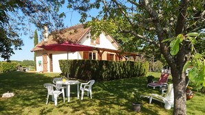 Una casa con techo rojo, fachada blanca y un césped bien cuidado. Hay una mesa con sillas y un paraguas rojo.