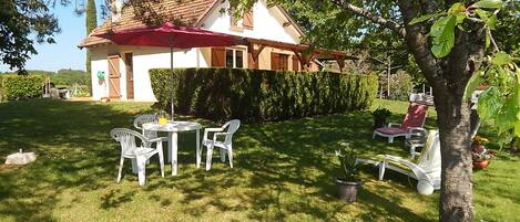 A house with a red roof, a white exterior, and a well-maintained lawn. There is a table with chairs and a red umbrella.