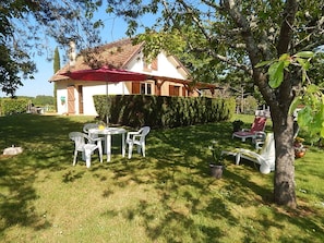 A house with a red roof, a white exterior, and a well-maintained lawn. There is a table with chairs and a red umbrella. - Quiet cottage (Martel)