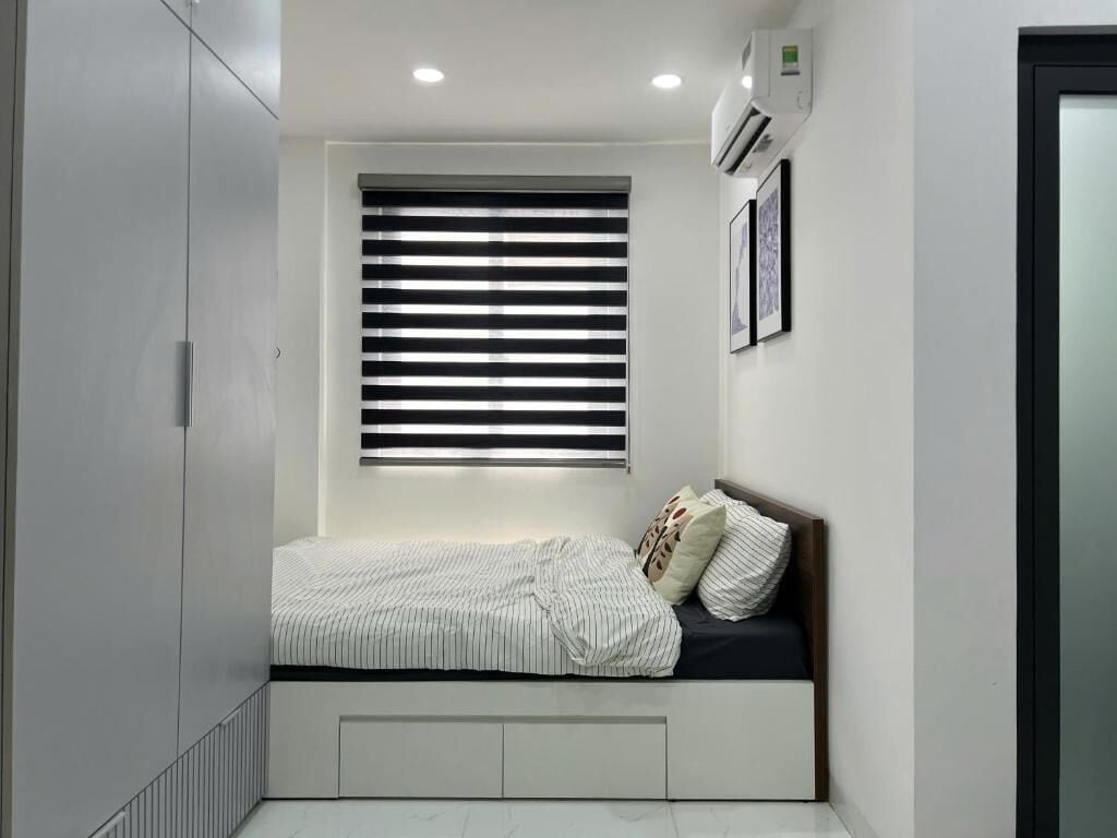 Une chambre à coucher comprenant un lit, des rangements intégrés, une fenêtre avec stores et un appareil de climatisation.