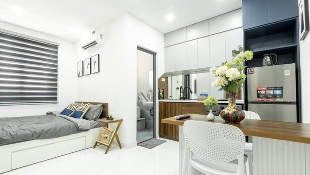 A compact room with a bed, kitchenette, and a dining area with a white chair. - Nhà Sài Gòn (Ho Chi Minh City)