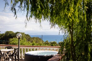 Eine Terrasse mit Tisch, Stühlen, einer Lampe und Blick aufs Meer.