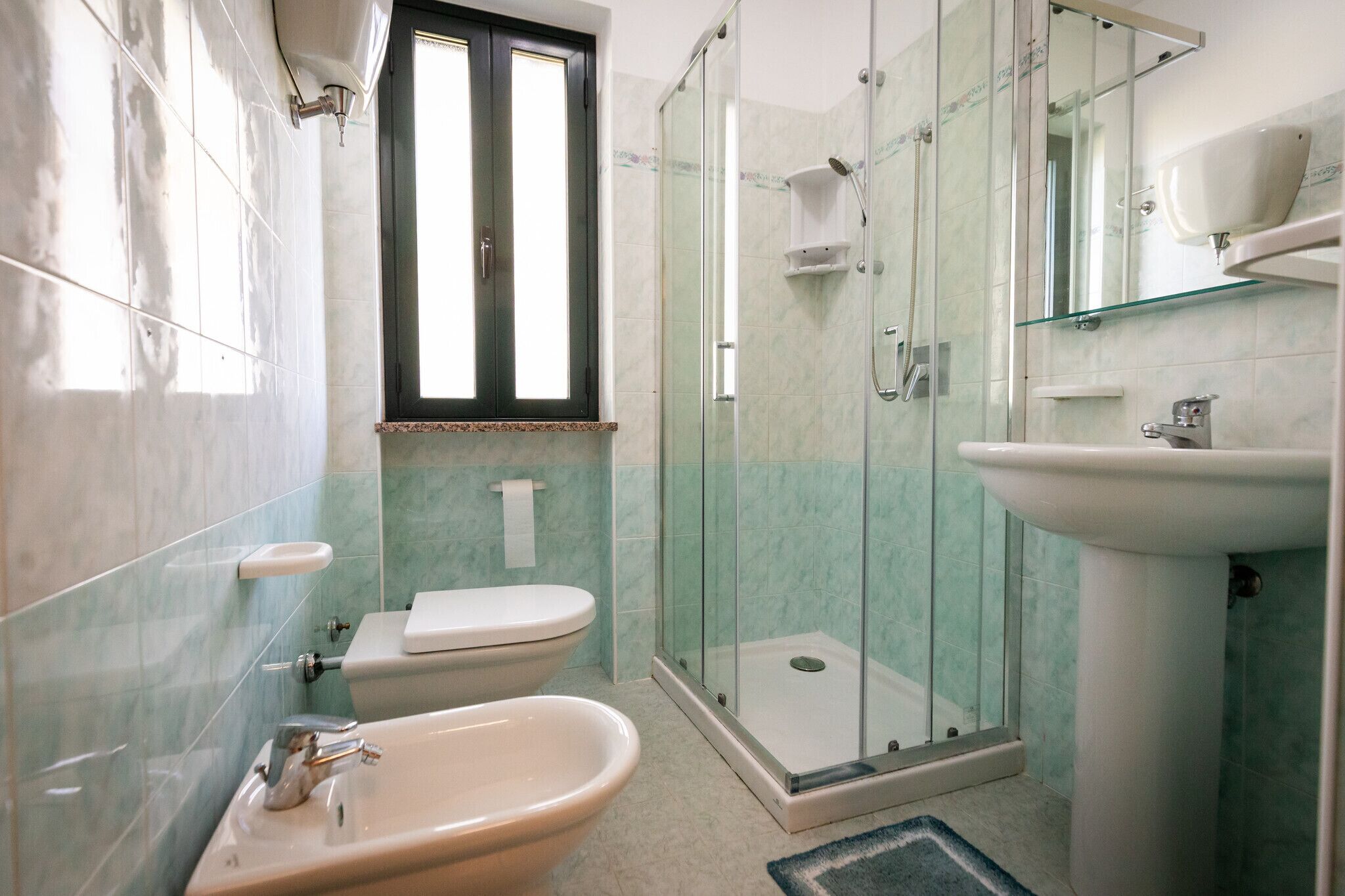 A bathroom with a toilet, bidet, sink, glass shower enclosure, and a mirror.