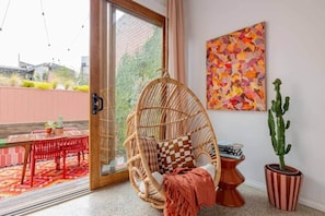 Ein Zimmer mit einem Korbstuhl, einer Kakteenpflanze und einem farbenfrohen abstrakten Gemälde.
