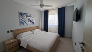 Hotelkamer met een bed, nachtkastje, plafondventilator, tv aan de muur en een raam met gordijnen.