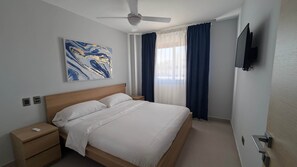 Ein Hotelzimmer mit Bett, Nachttisch, Deckenventilator, Wandfernseher und einem Fenster mit Vorhängen.
