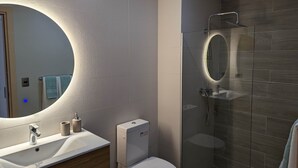 Een moderne badkamer met een grote spiegel, een toilet, een wastafel en een douchecabine van glas.