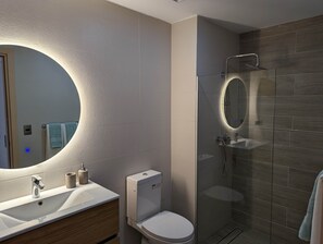 Ein modernes Badezimmer mit großem Spiegel, Toilette, Waschbecken und einer Duschkabine aus Glas.