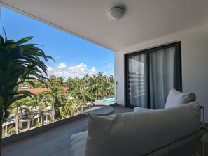 Ein Balkon mit Blick auf Palmen und einen Swimmingpool, ein weißes Sofa und ein runder Tisch.
