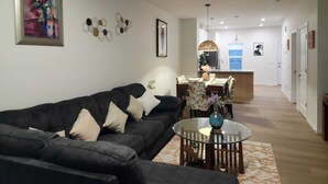 Ein Wohnzimmer mit einer Couch, einem runden Glastisch und einem Essbereich mit Stühlen.