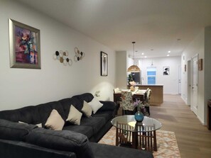 Ein Wohnzimmer mit einer Couch, einem runden Glastisch und einem Essbereich mit Stühlen.