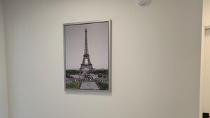 Ein Zimmer mit einem gerahmten Bild des Eiffelturms an der Wand, einer weißen Decke und einem Teppichboden.