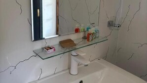 A bathroom with a white sink, a glass shelf with toiletries, a mirror, and a window with a black frame. - Full Moon Hotel (Nuwara Eliya)