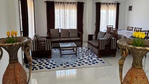 A living room with a sofa, armchairs, a coffee table, patterned curtains, and decorative vases with flowers. - Full Moon Hotel (Nuwara Eliya)