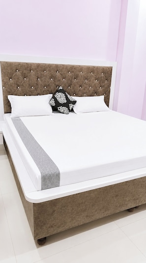 Una cama con cabecera capitonada, ropa de cama blanca y almohadas estampadas.