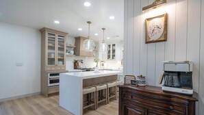 A kitchen with a central island, bar stools, a coffee maker, and wooden cabinets. - Mountain Luxury Retreat (Orem)
