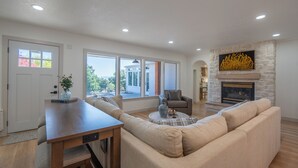 A living room with a stone fireplace, a sofa, a dining table, and large windows. - Mountain Luxury Retreat (Orem)