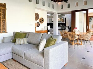 Ein modernes Wohnzimmer mit grauem Sofa, Korbstühlen und einem Essbereich mit Tisch und Stühlen.