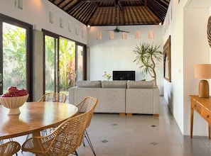 Ein modernes Wohnzimmer mit einer Couch, einem Esstisch mit Stühlen, einem Fernseher und einem Deckenventilator.