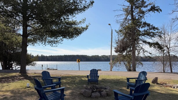 A lakeside seating area with Adirondack chairs, a fire pit, and a clear view of the lake.