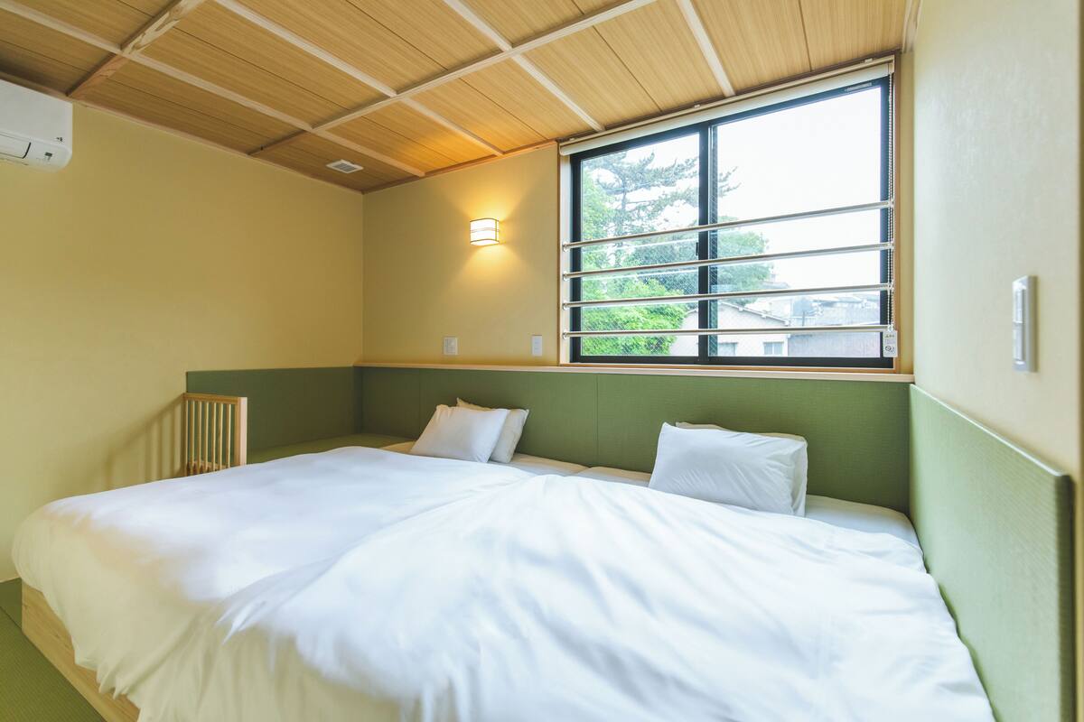 Ein Zimmer mit einem Bett, einem Fenster mit Jalousien, einer Wandleuchte und einer Heizung.