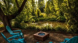 A seating area with chairs and a table, surrounded by trees and a body of water. - Crater Lake Themed Retreat in Eagle Point (Eagle Point)