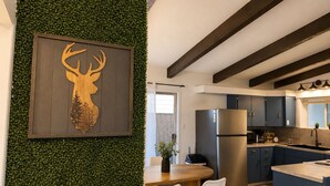 A modern kitchen with a central island, dark wooden beams, and a green wall with a deer head decoration. - Crater Lake Themed Retreat in Eagle Point (Eagle Point)