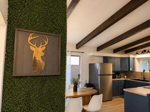 Eine moderne Küche mit einer zentralen Kochinsel, dunklen Holzbalken und einer grünen Wand mit Dekoration in Form eines Hirschkopfes.